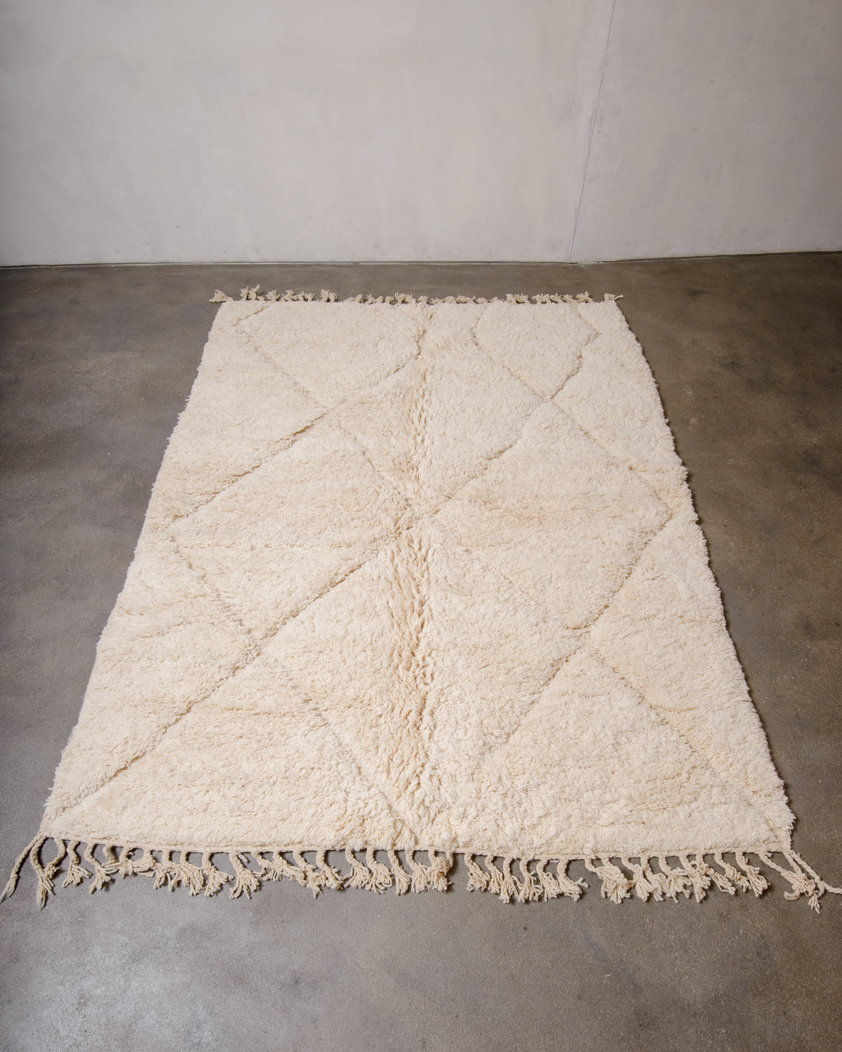 Cream wool Beniourain rug laying flat on concrete floor.